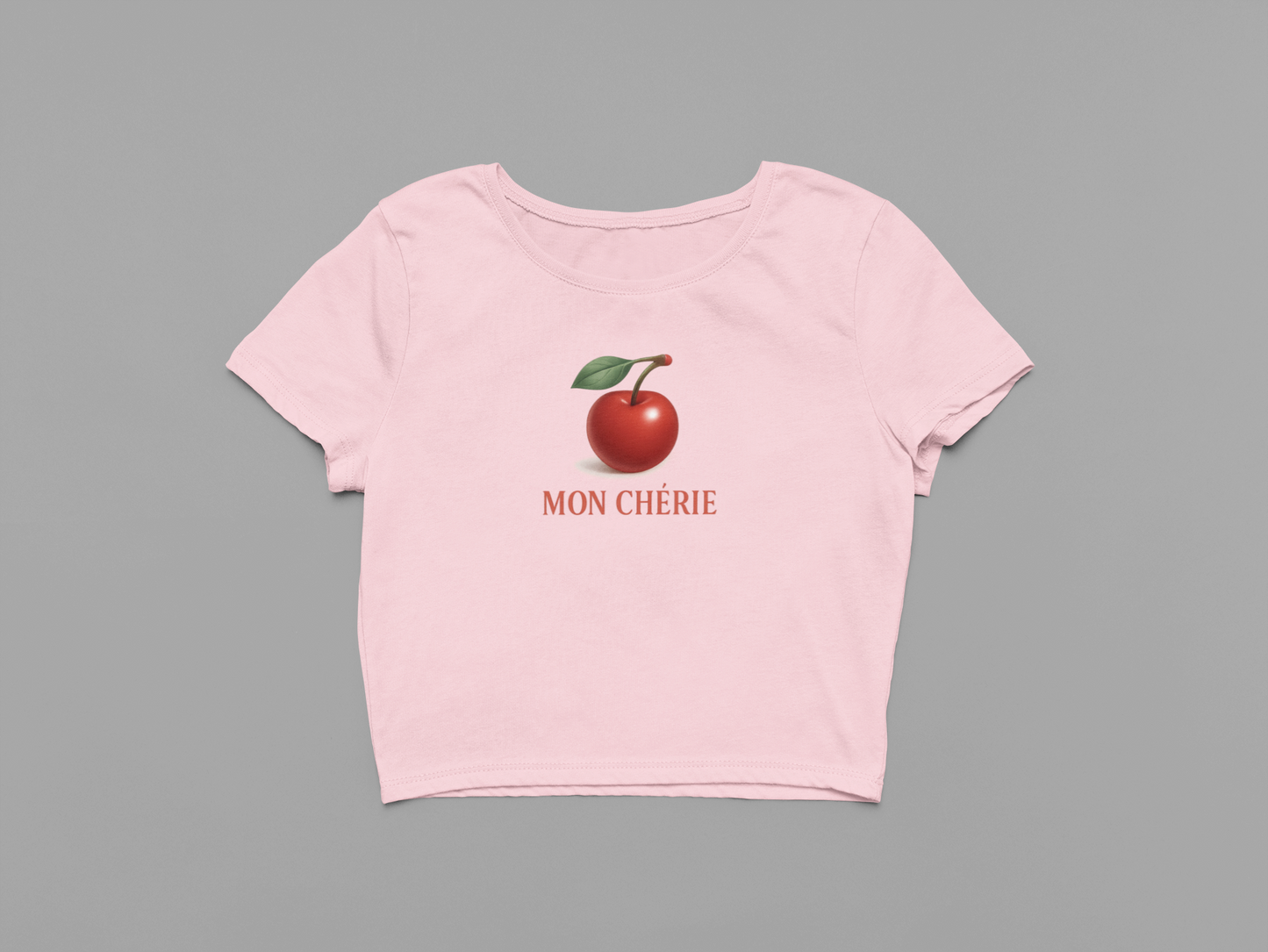 Pink t-shirt with a red apple graphic and 'MON CHERIE' text on a gray background